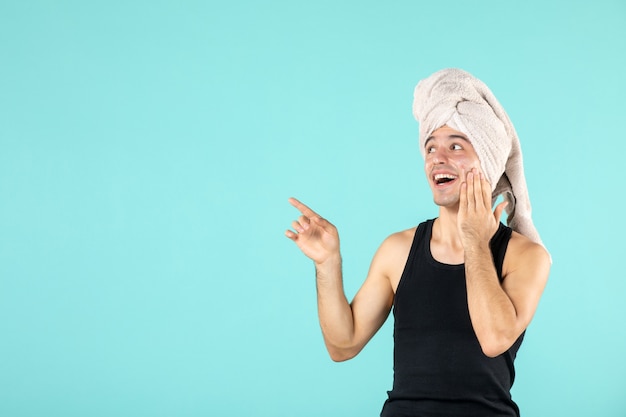 Free Photo front view of young man after shower applying cream to his face on blue wall