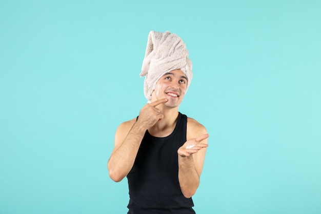 Free Photo front view of young man after shower applying mask on his face on blue wall