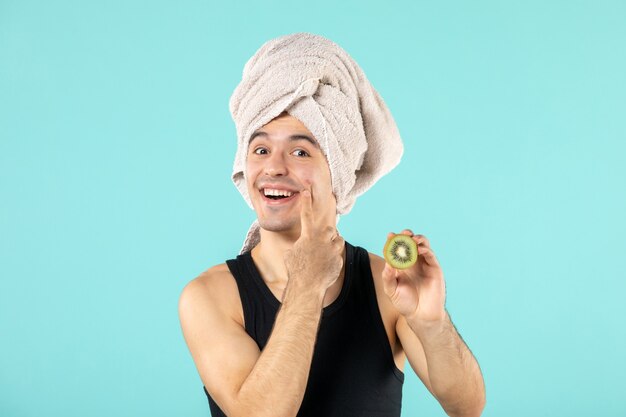 front view of young man after shower holding kiwi slices on blue wall