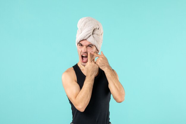 front view of young man after shower trying to squeeze out little pimple on blue wall