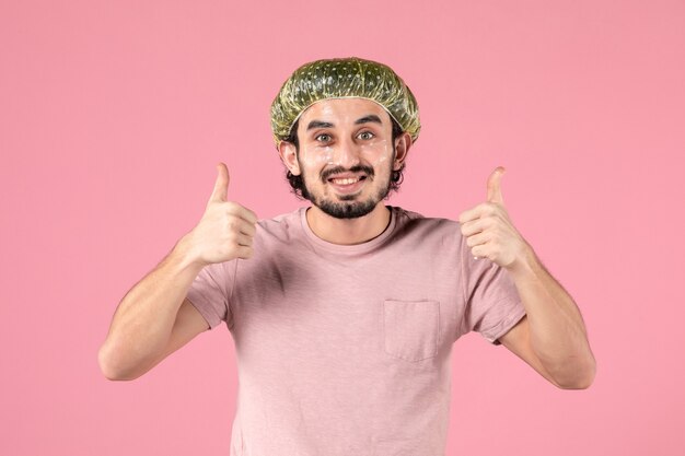 front view of young man applying mask on his face on pink wall