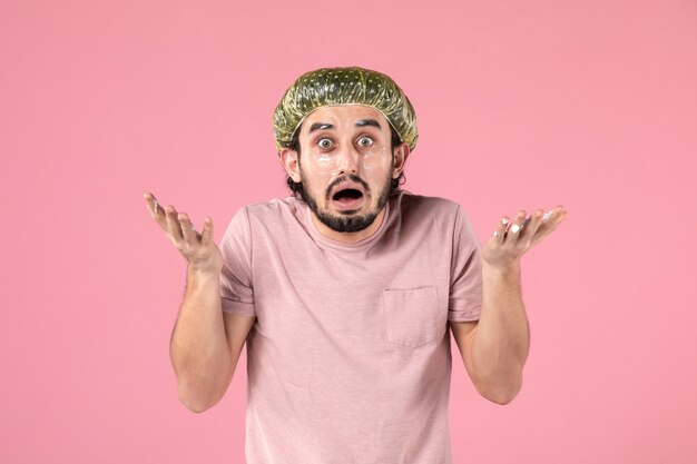 front view of young man applying mask on his face on pink wall