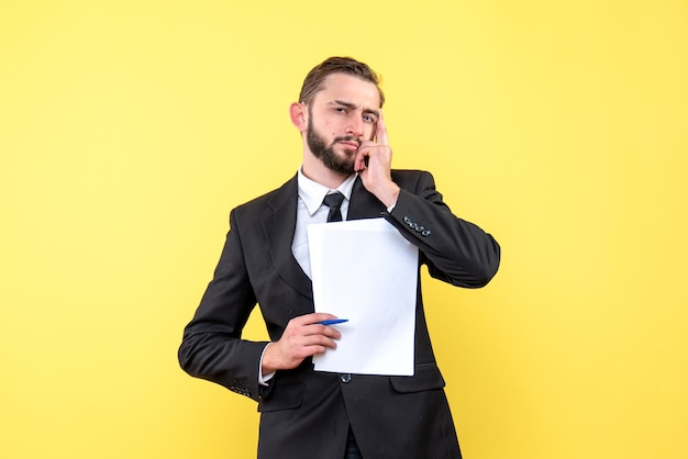 Front view of young man in black suit looks up thoughtfully holding a hand near his face on yellow