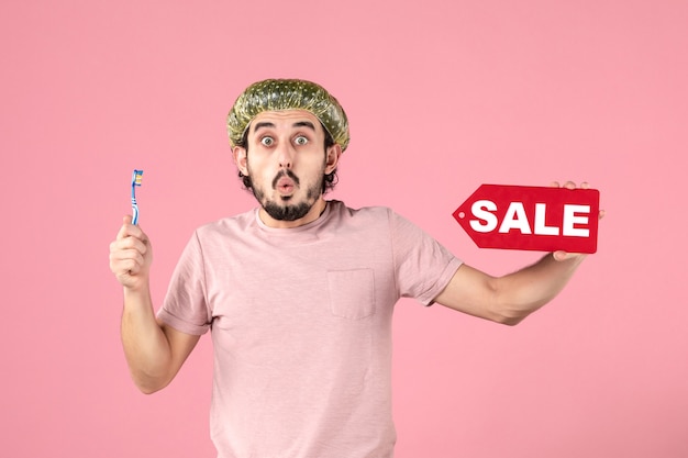 Free photo front view of young man cleaning his teeth and holding sale banner on pink wall