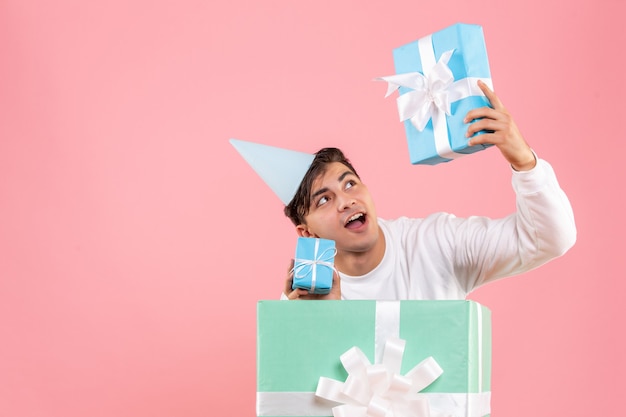 Free photo front view of young man hiding inside present and holding other presents on pink wall