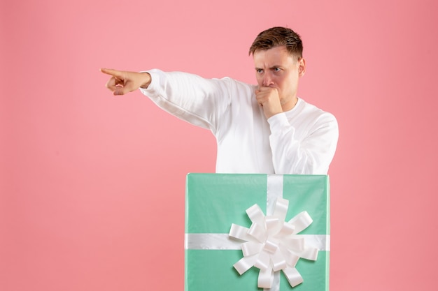 Free photo front view of young man hiding inside present on pink wall