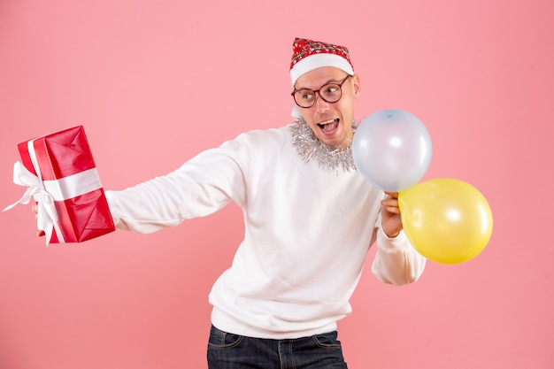 Free photo front view of young man holding balloons and present on pink wall