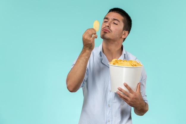 Front view young man holding basket with cips on a blue desk film remote movies cinema male