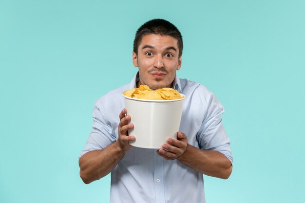 Front view young man holding basket with cips on blue desk film remote movies cinema theater