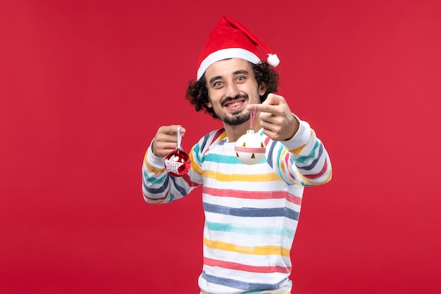 Free Photo front view young man holding christmas tree toys on red wall new year red holiday