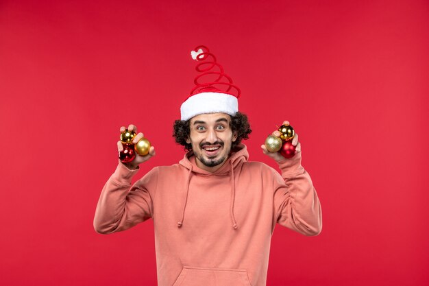 Free Photo front view of young man holding christmas tree toys on red wall