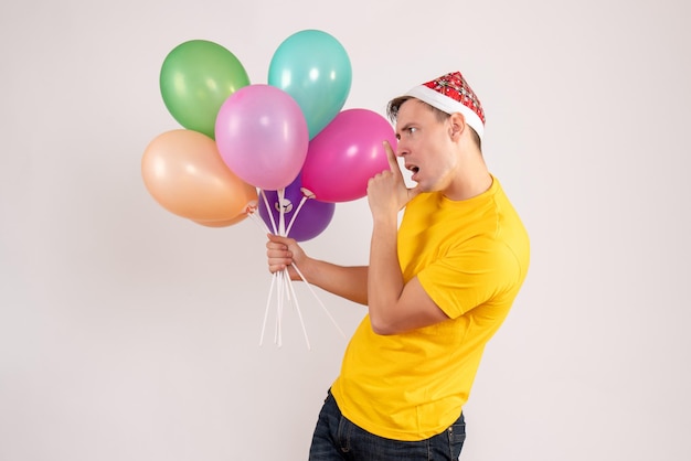 Front view of young man holding colorful balloons on a white wall