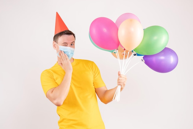 Front view of young man holding colorful balloons on the white wall