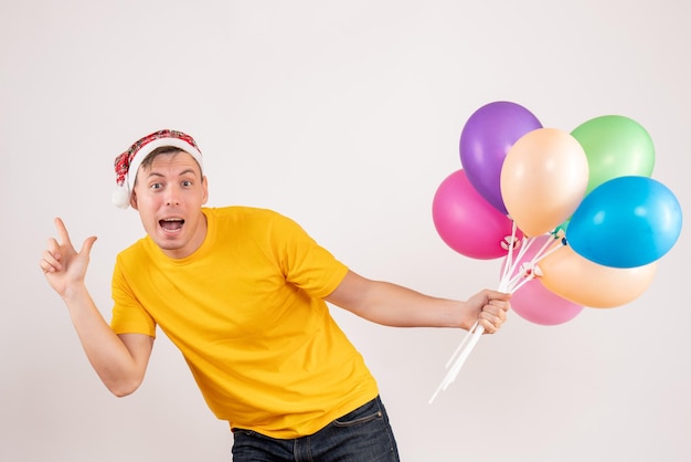 Front view of young man holding colorful balloons on the white wall