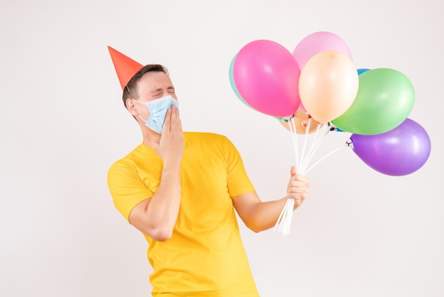 Front view of young man holding colorful balloons on white wall