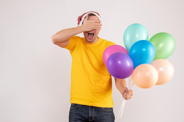 Front view of young man holding colorful balloons on white wall