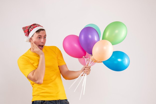 Front view of young man holding colorful balloons on white wall