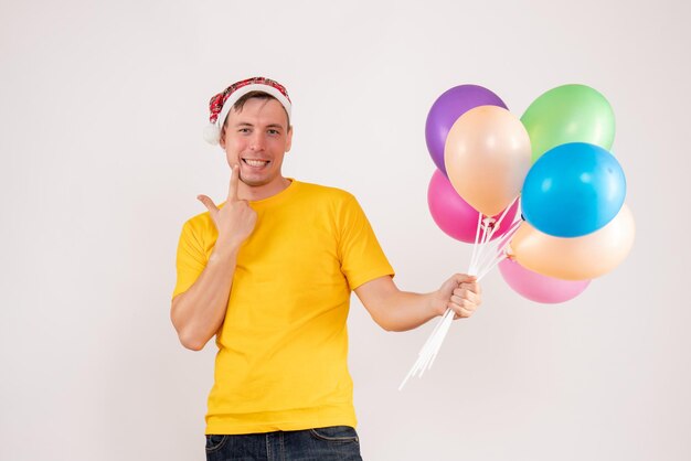 Front view of young man holding colorful balloons on white wall