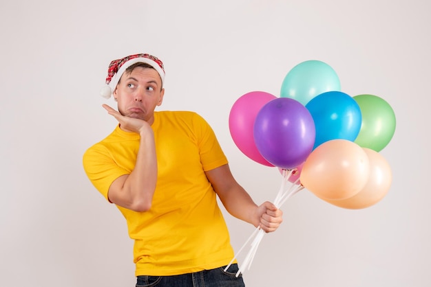 Free photo front view of young man holding colorful balloons on white wall