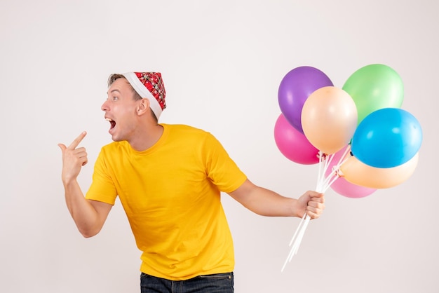 Front view of young man holding colorful balloons on white wall