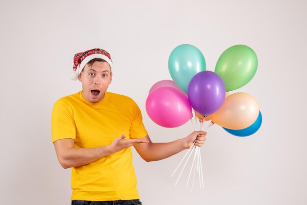 Front view of young man holding colorful balloons on a white wall