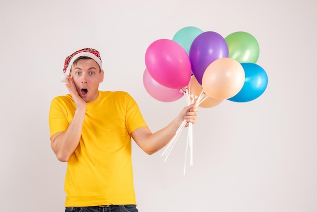 Front view of young man holding colorful balloons on white wall