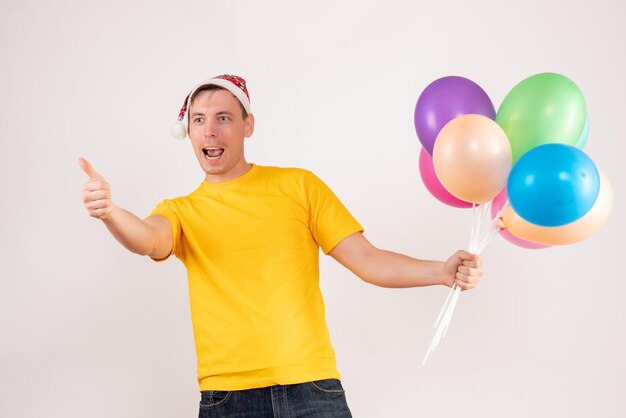 Front view of young man holding colorful balloons on white wall