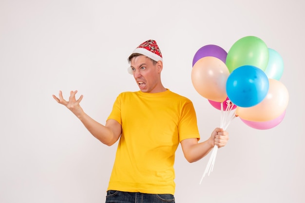 Front view of young man holding colorful balloons on white wall