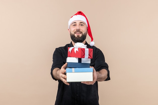 Front view of young man holding holiday presents on pink wall