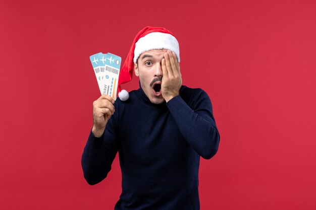 Front view young man holding plane tickets on a red background