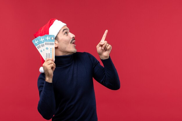 Front view young man holding plane tickets on red background