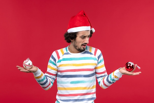 Free Photo front view young man holding plastic toys on a red wall red human holiday new year