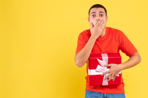 Front view of young man holding present shocked on yellow wall