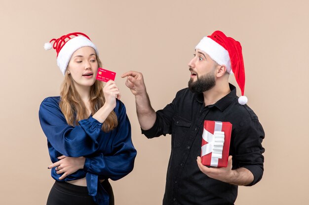 Front view of young man holding present with woman who's holding bank card on pink wall