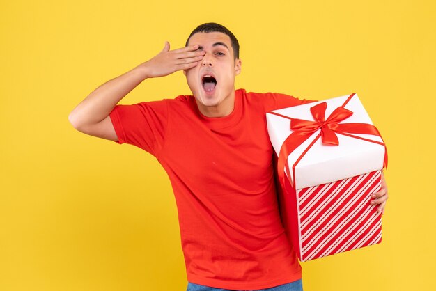 Front view of young man holding present on a yellow wall