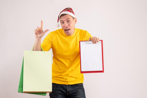 Front view of young man holding shopping packages and note on the white wall