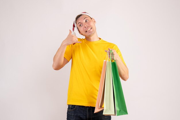 Front view of young man holding shopping packages on white wall