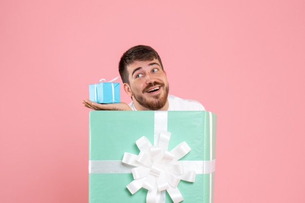 Free photo front view of young man inside present box holding little gift on pink wall