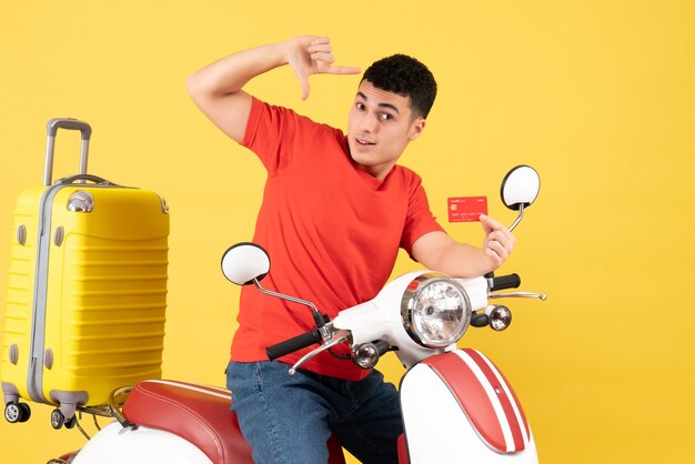 Front view young man on moped with yellow suitcase holding card