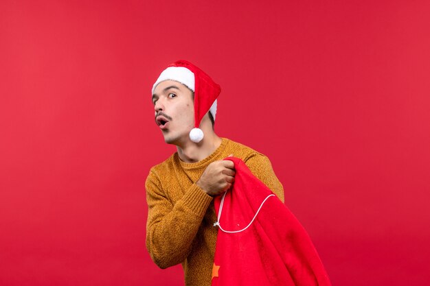 Front view of young man opening present bag on red wall