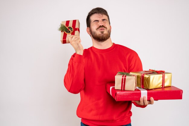 Front view of young man in red shirt holding christmas presents on white wall