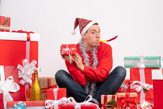 Front view of young man sitting around xmas presents on the white wall