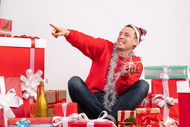 Front view of young man sitting around xmas presents on white wall