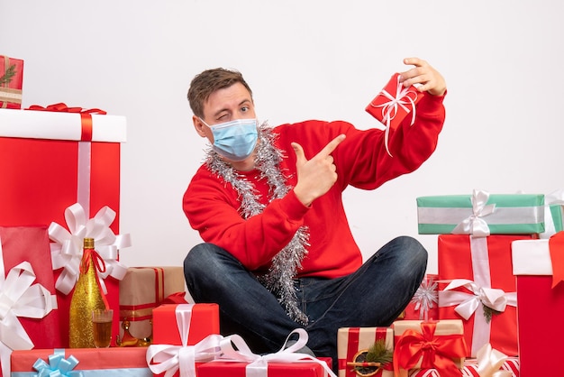 Front view of young man in sterile mask sitting around xmas presents on a white wall