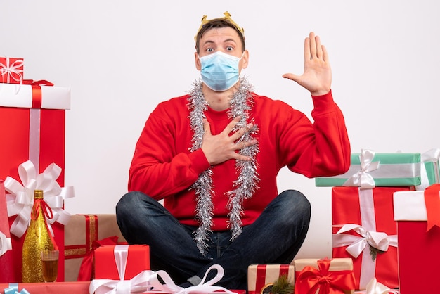 Front view of young man in sterile mask sitting around xmas presents on the white wall