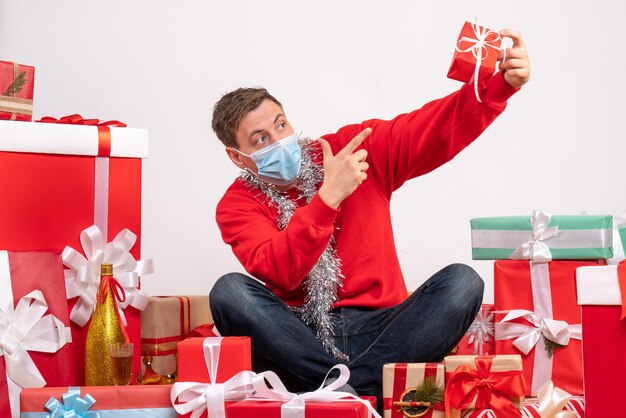 Front view of young man in sterile mask sitting around xmas presents on the white wall