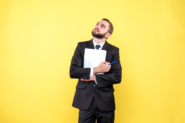 Free Photo front view of young man thoughtful businessman wearing suit looking up and holding blank paper with a pen on yellow