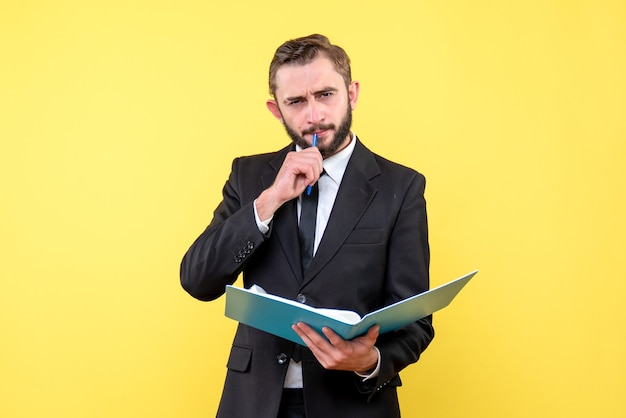 Front view of young man thoughtfully businessman touching pen to his mouth holds blue folder on yellow