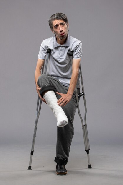 Front view young man using crutches due to broken foot on grey floor disable leg foot broken accident