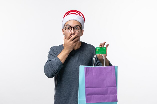 Front view of young man with bank card and packages on white wall